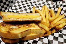A grilled cheese sandwich and french fries on a checkered paper.