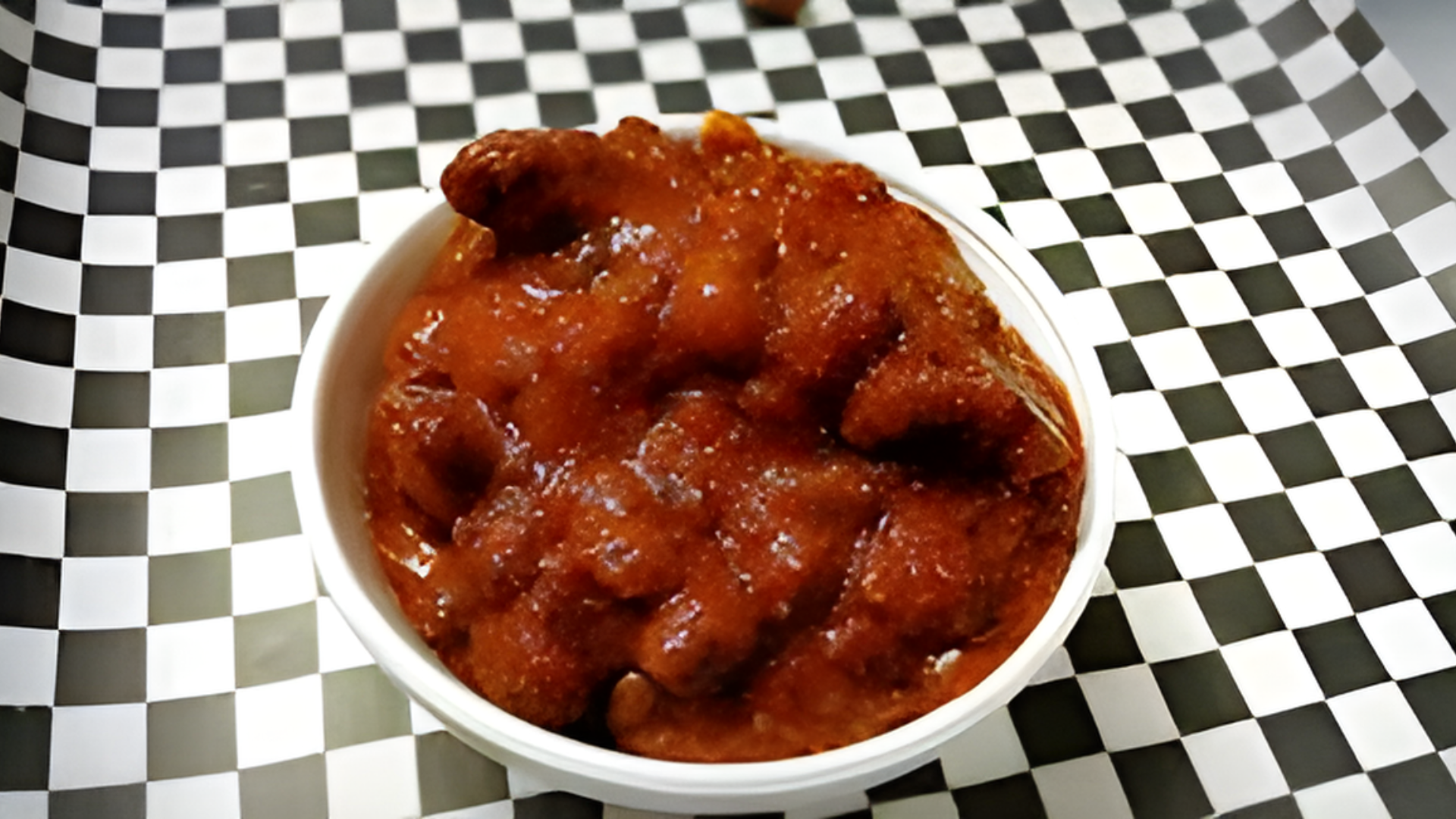 A bowl of chili is sitting on a checkered table cloth.