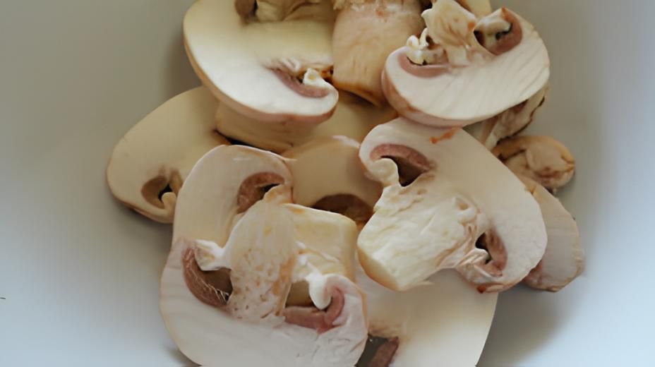 A white bowl filled with sliced mushrooms on a table.