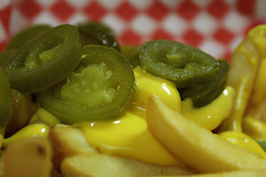 A close up of a plate of french fries with cheese and jalapenos.