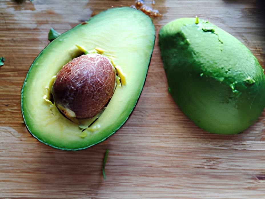 Two avocados are cut in half on a wooden cutting board.