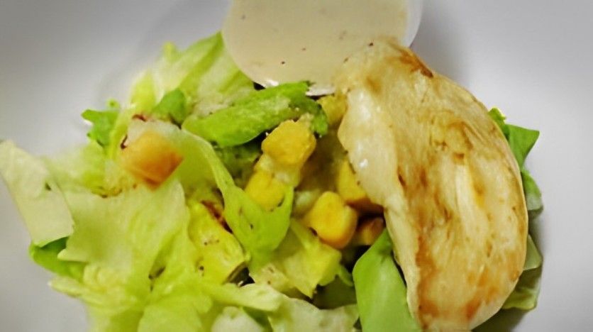 A close up of a salad with chicken , lettuce , corn and dressing in a bowl.