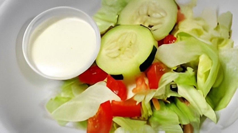 A salad with lettuce tomatoes cucumbers and ranch dressing on a plate