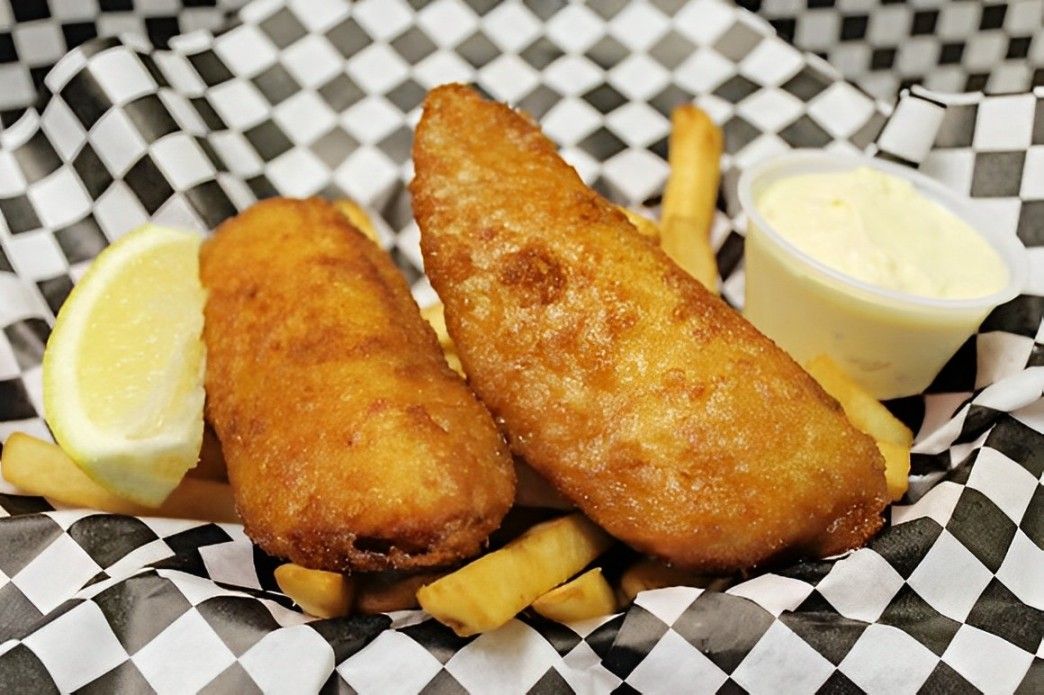 Two pieces of fish and french fries in a basket on a checkered paper.