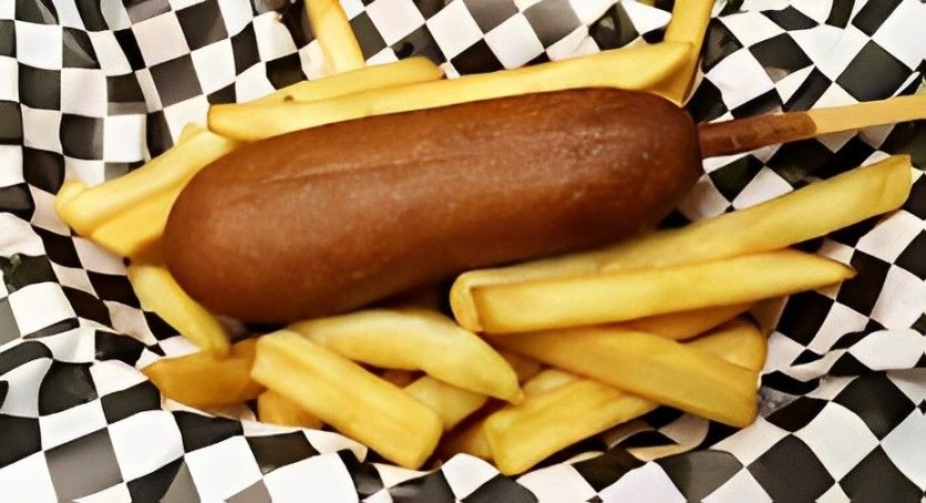 A corn dog and french fries on a checkered paper.