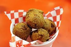 A bowl of falafel balls wrapped in checkered paper on an orange table.