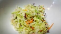 A close up of a bowl of coleslaw with carrots and cabbage.