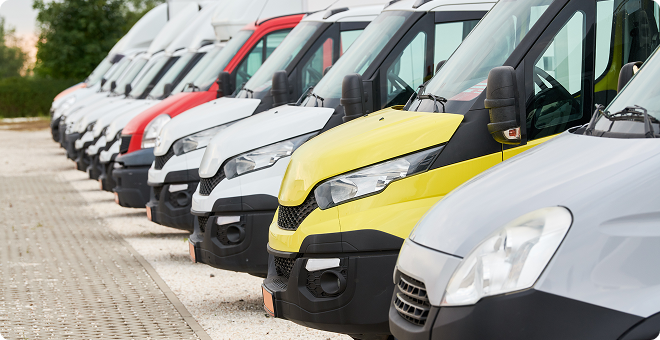 Row of parked vans in white, red, yellow, and gray along a paved lot | The Recon Garage