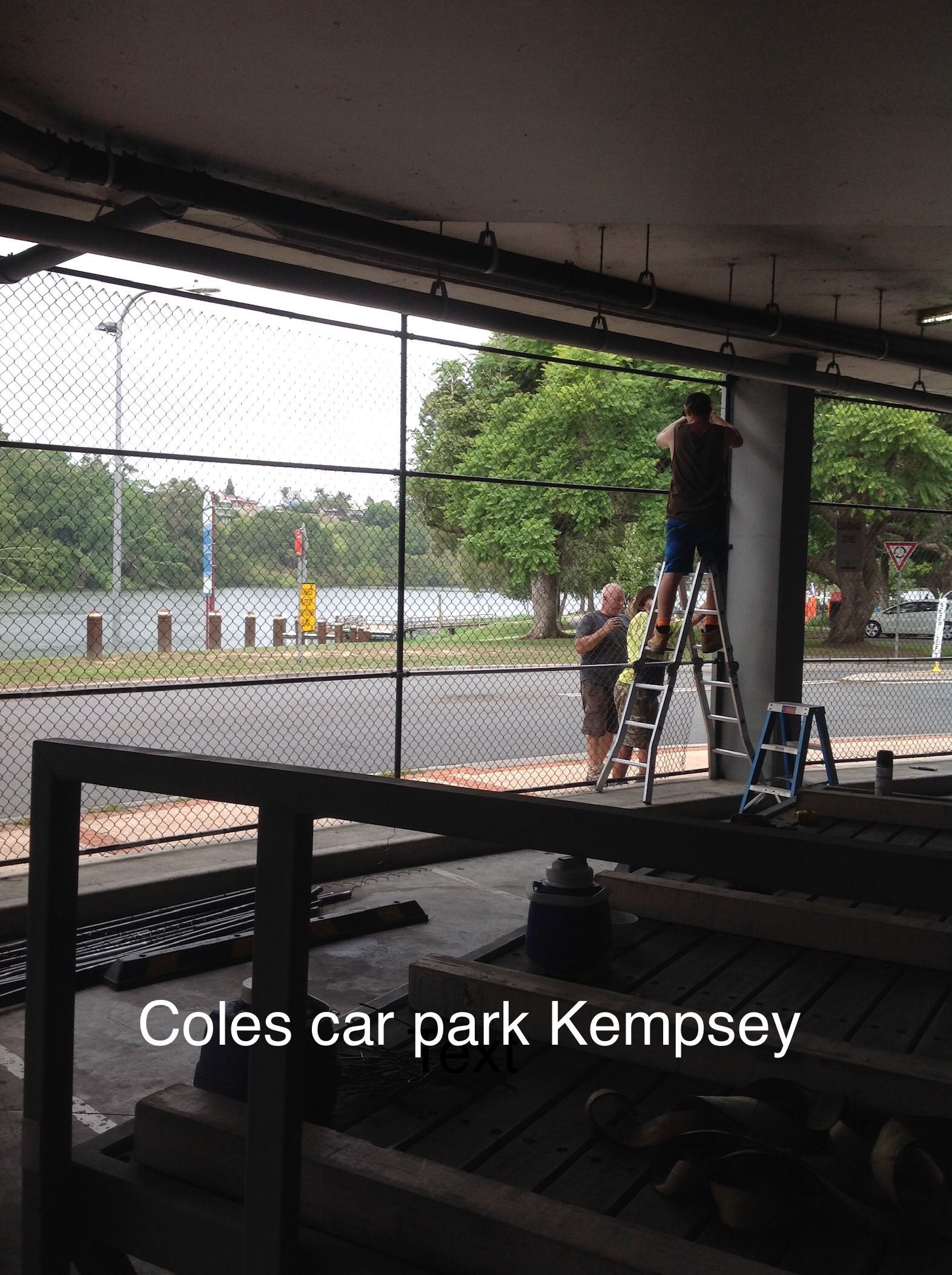 Two people on ladders work in a Coles car park near water — Fencer Steve In Temagog, NSW
