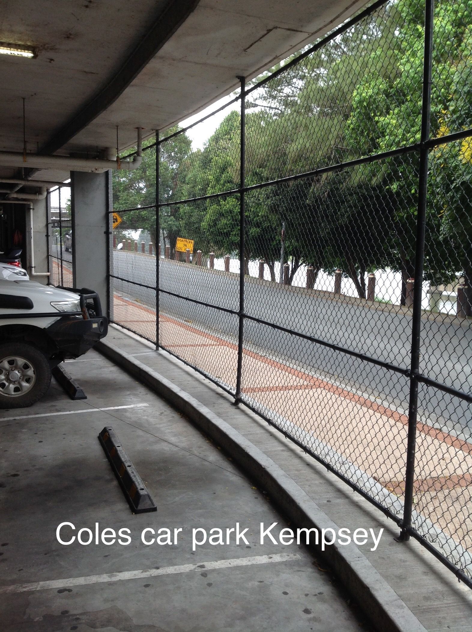 Coles car park, Kempsey: Black netting along an open-air parking area, with a street and trees visible in the background — Fencer Steve In Temagog, NSW