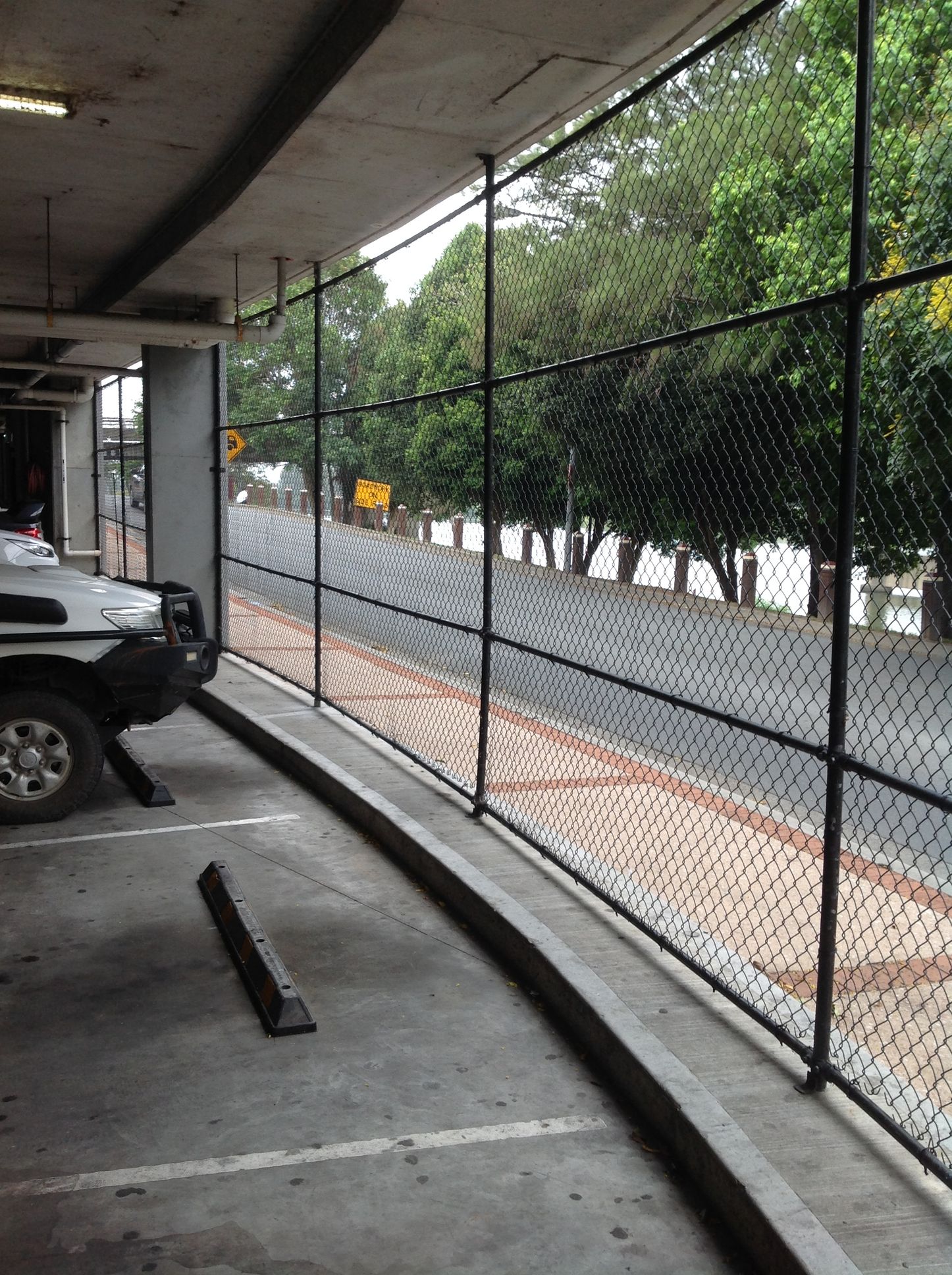 Black Fence Along a Parking Structure, With a Street and Trees in the Background — Fencer Steve In Hat Head, NSW