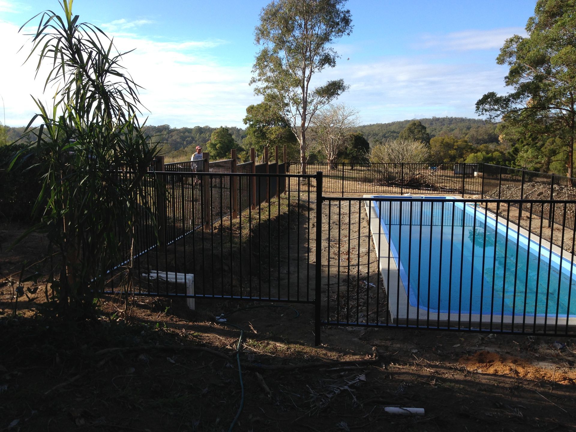 Black fence surrounds a pool in a sunny outdoor setting with hills and trees in the distance — Fencer Steve In Temagog, NSW