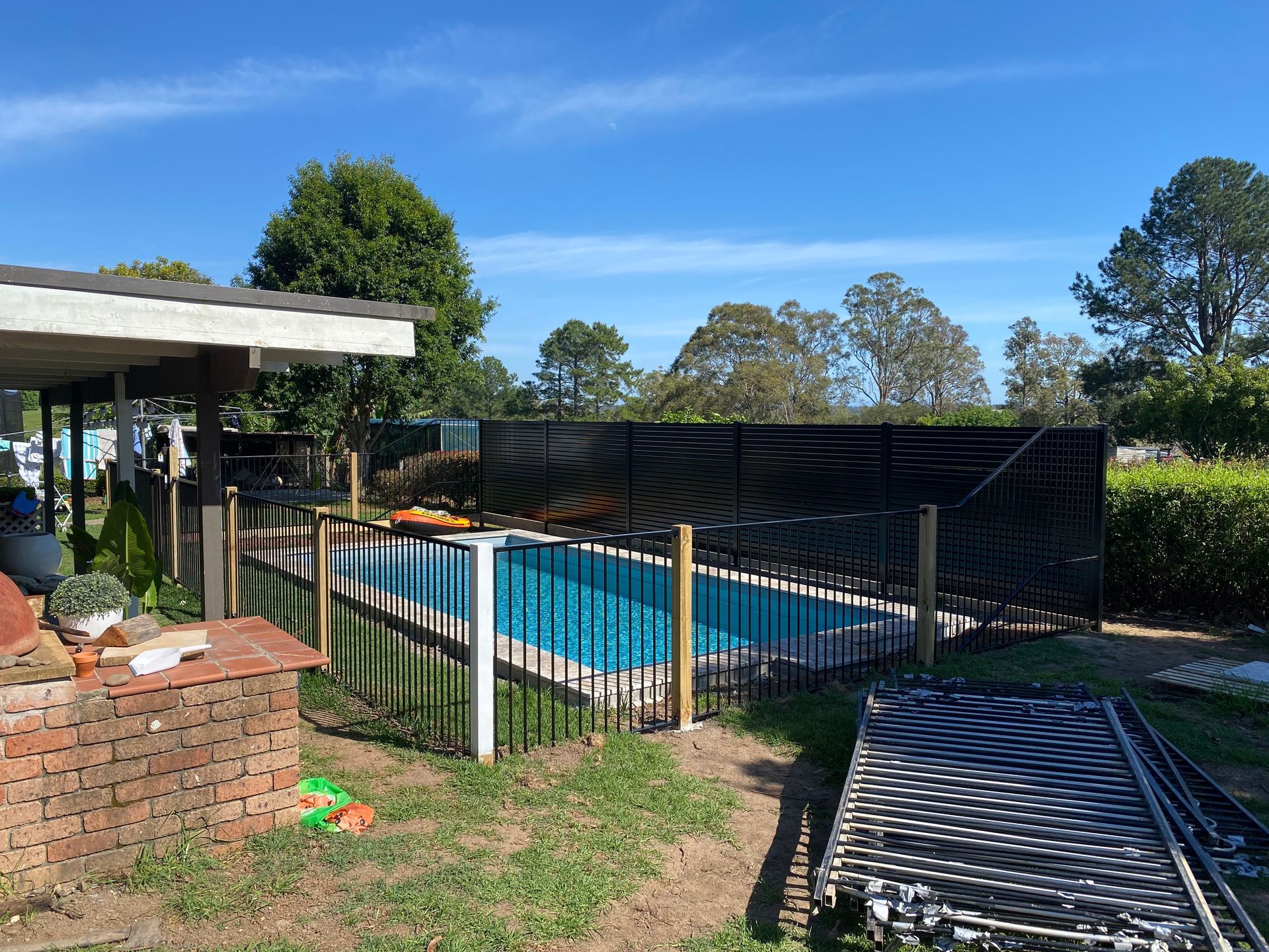 Pool fenced in backyard with blue water, black fence, and sunny sky — Fencer Steve In Temagog, NSW