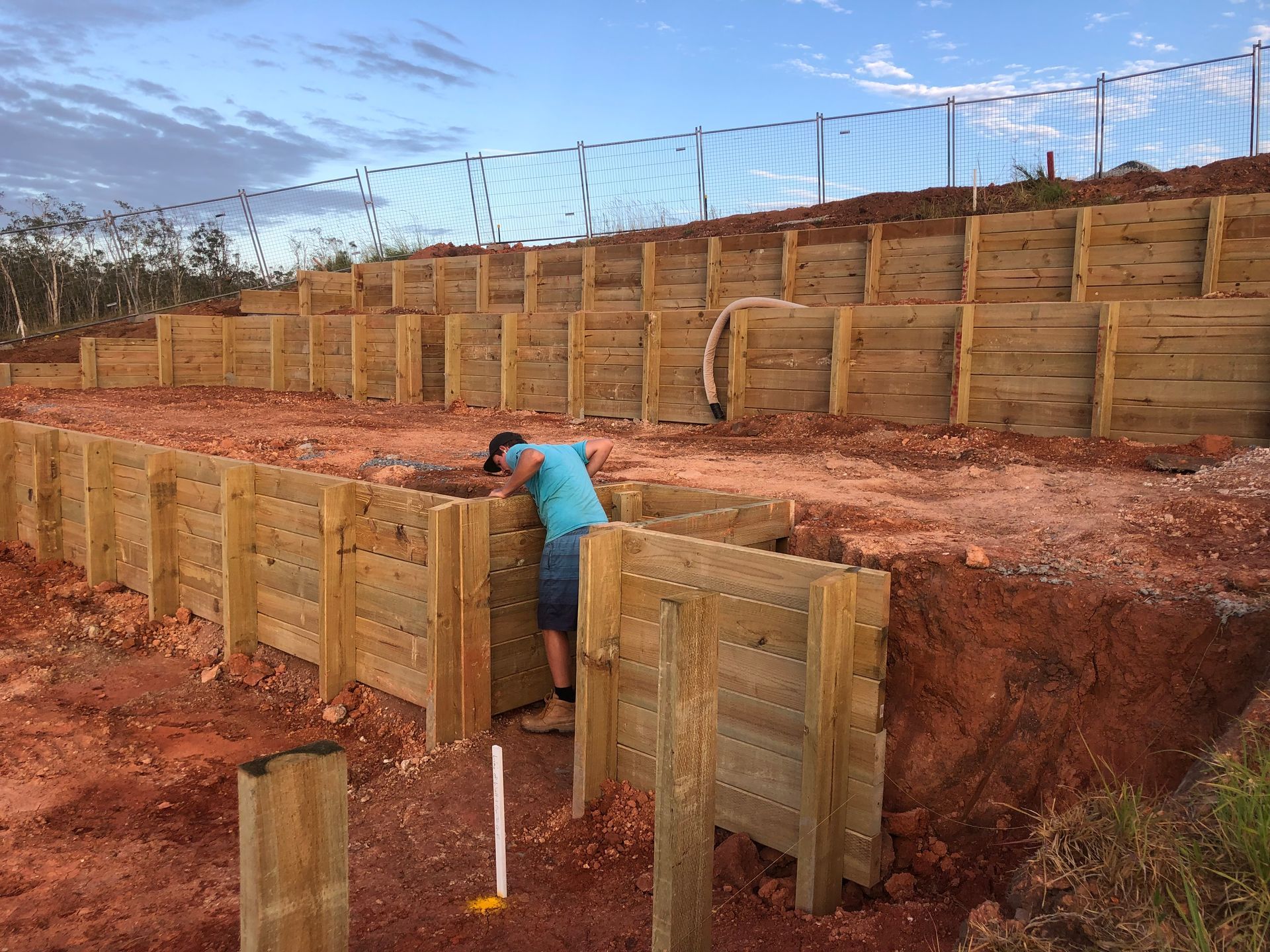 Man Constructing a Tiered Wooden Retaining Wall on a Hillside — Fencer Steve In Crescent Head, NSW