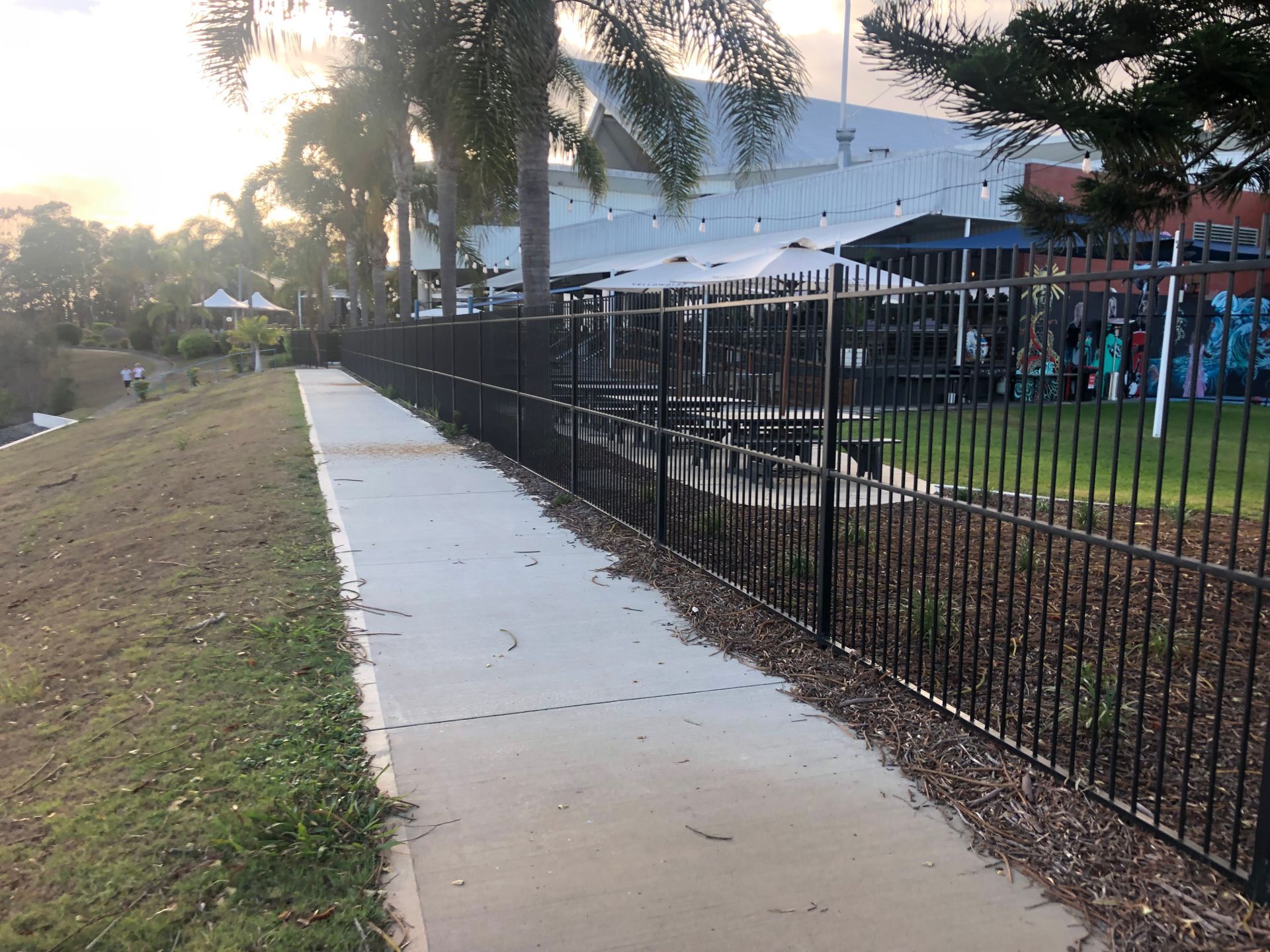 A black metal fence lines a concrete path, with grass to the left and a building in the background — Fencer Steve In Temagog, NSW