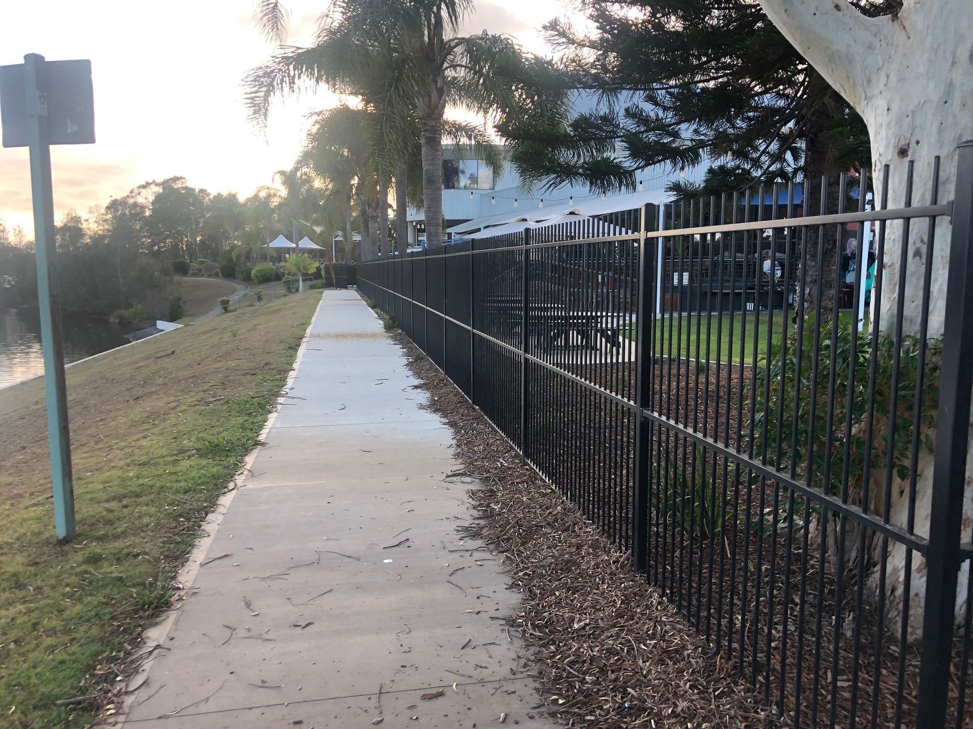 Concrete Pathway Next to a Black Fence, Grassy Bank, and Body of Water — Fencer Steve In Temagog, NSW