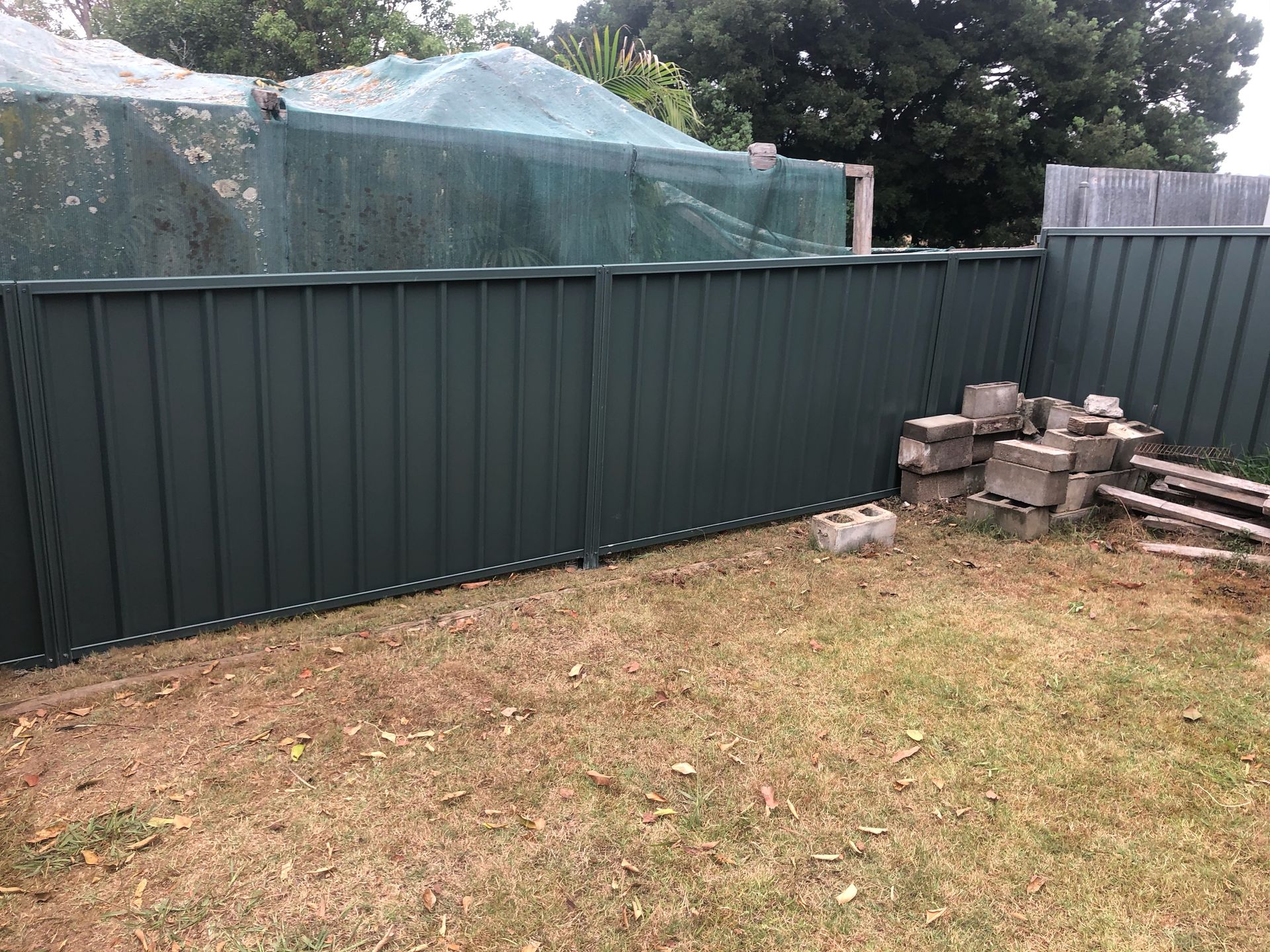 Green metal fence in a backyard with dry grass and concrete blocks — Fencer Steve In Temagog, NSW