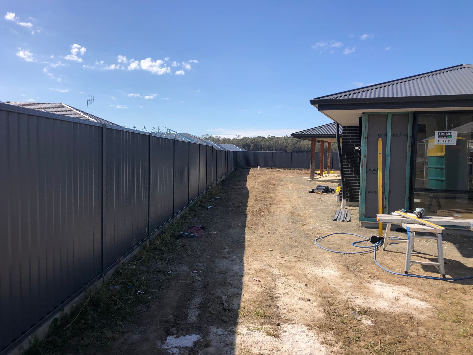 Gray metal fence beside a dirt driveway with a house under construction, blue sky — Fencer Steve In Temagog, NSW