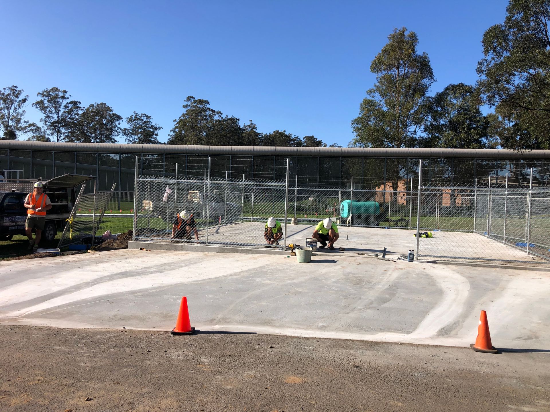 Construction workers installing a chain-link fence on a concrete pad outdoors under a blue sky — Fencer Steve In Temagog, NSW