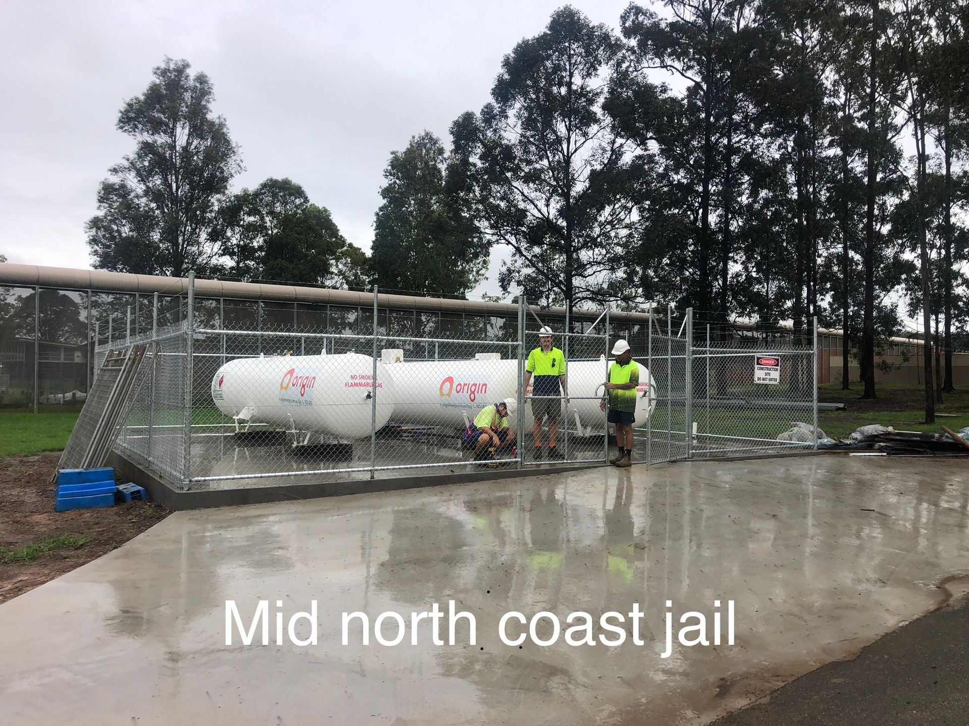 Two white tanks behind a chain-link fence at the Mid North Coast jail, with three workers in safety gear — Fencer Steve In Temagog, NSW