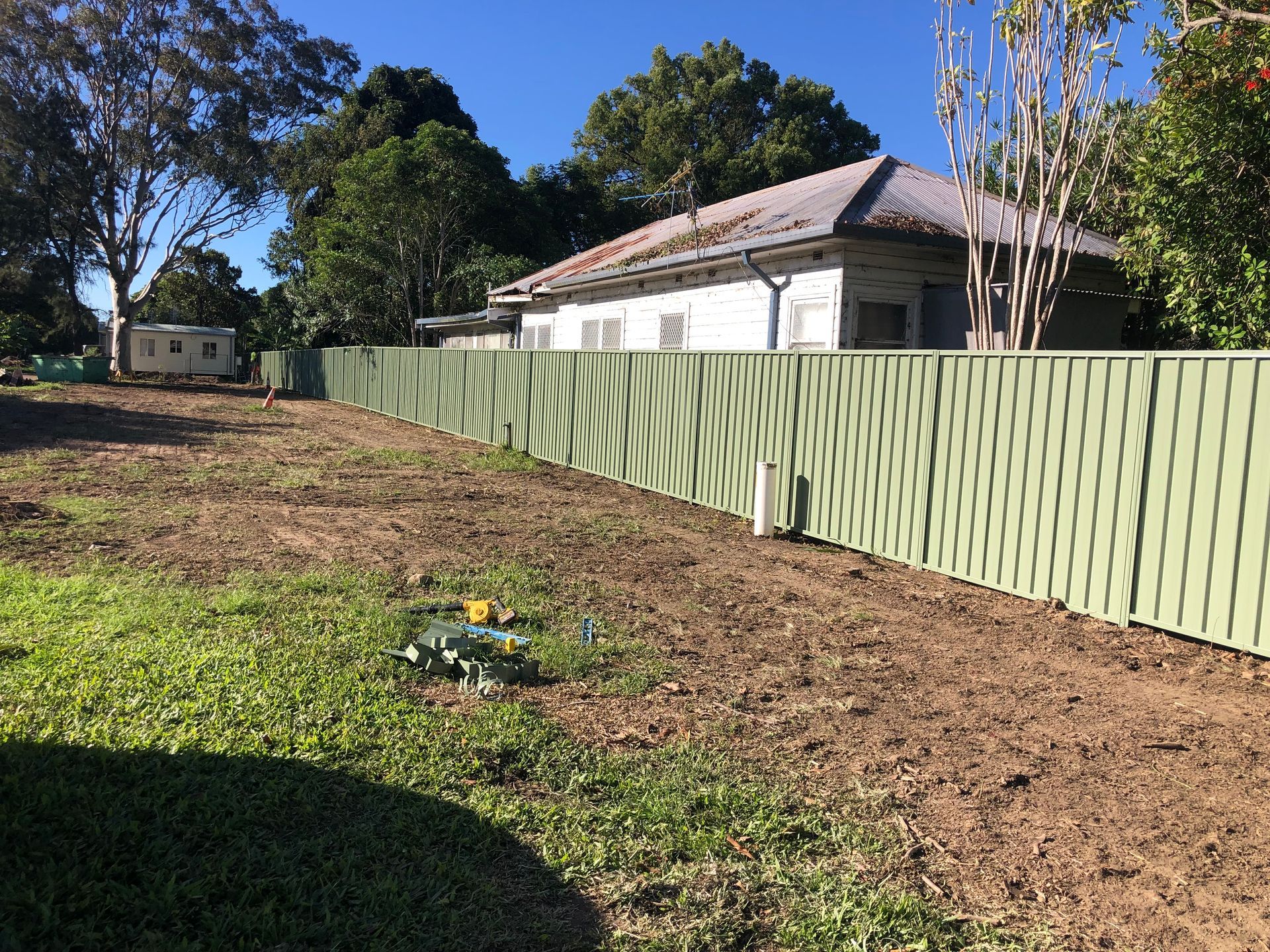 Green Corrugated Fence in a Yard With a House in the Background and Blue Sky — Fencer Steve In Temagog, NSW