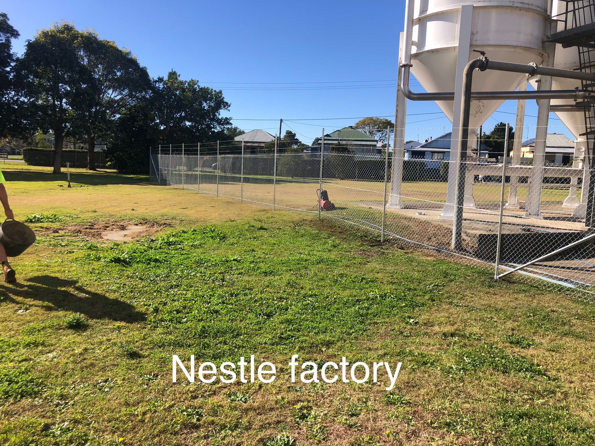 Nestle factory with silos, green grass, and a person carrying a bag. Fenced area in front — Fencer Steve In Temagog, NSW