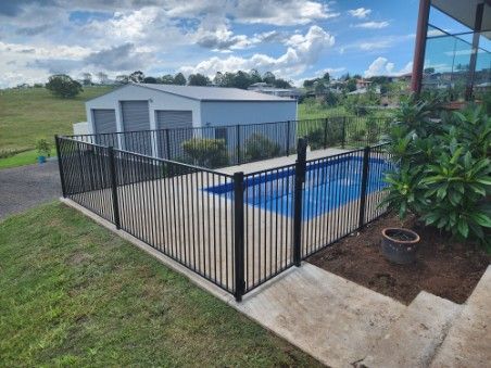 Black fenced-in pool in a yard, with a shed in the background. Blue water, green grass and shrubs — Fencer Steve In Temagog, NSW