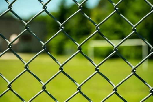 Chain-link Fence in Focus, Obscuring a Blurry View of a Green Field and Soccer Goal — Fencer Steve In Wauchope, NSW