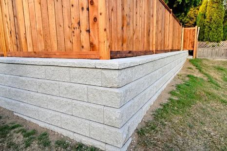 Gray Stone Retaining Wall Supports a Wooden Fence, With Green Grass Surrounding It — Fencer Steve In South West Rocks, NSW