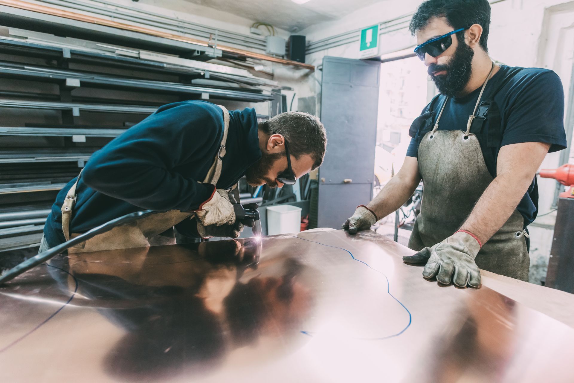 Two metalworkers are performing a sheet metal cutting at the forge workbench. Two metalworkers are performing a sheet metal cutting at the forge workbench.