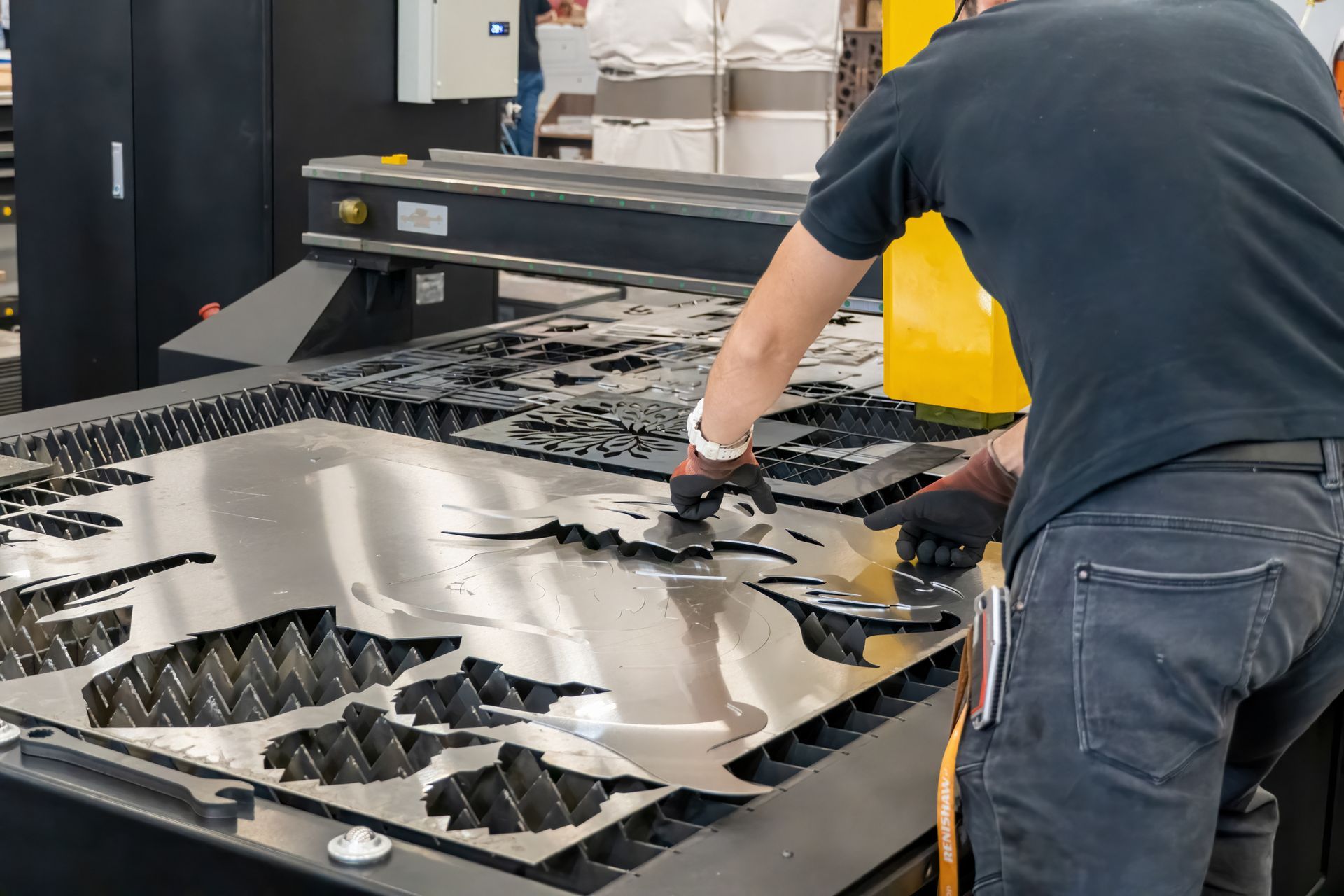 A partial view of a technician removing metal from a metal sheet on a laser cutting machine.