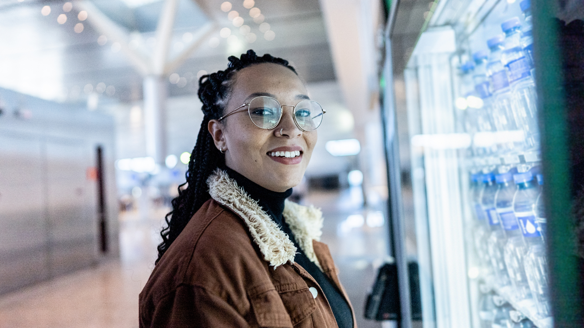Smiling person in glasses beside a brightly lit refrigerated display in a store aisle