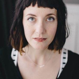 A woman with short hair is wearing a black shirt and a necklace.