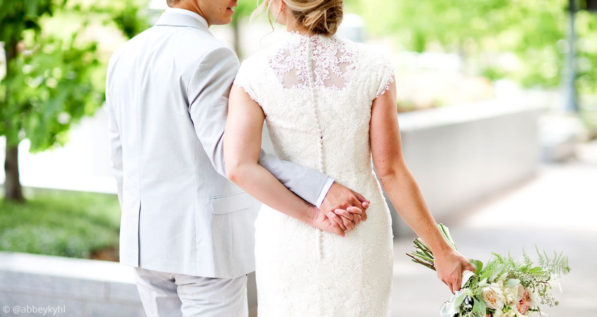 A bride and groom are holding hands while walking down the street.