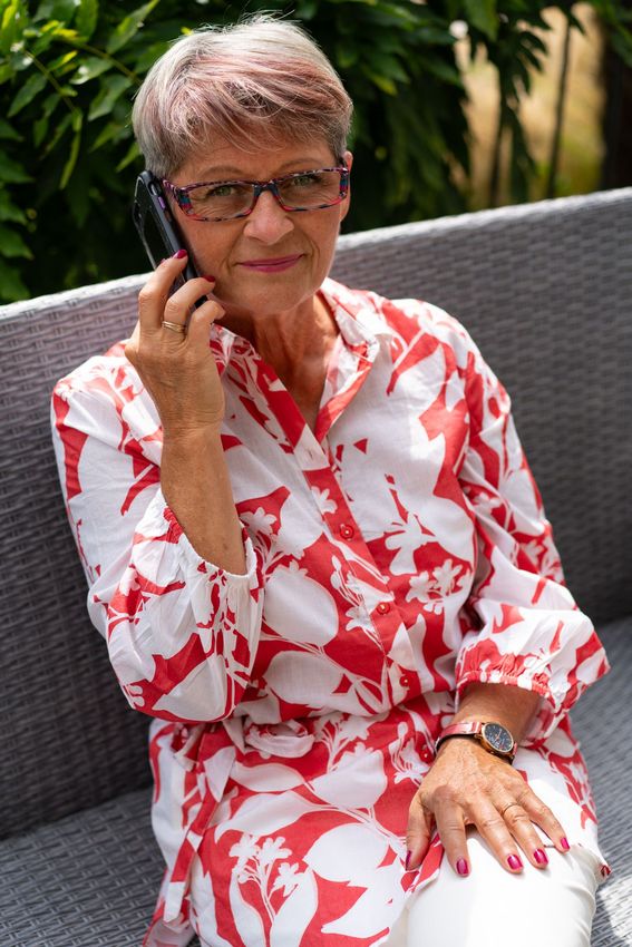 Une femme âgée est assise sur un canapé et parle au téléphone portable.