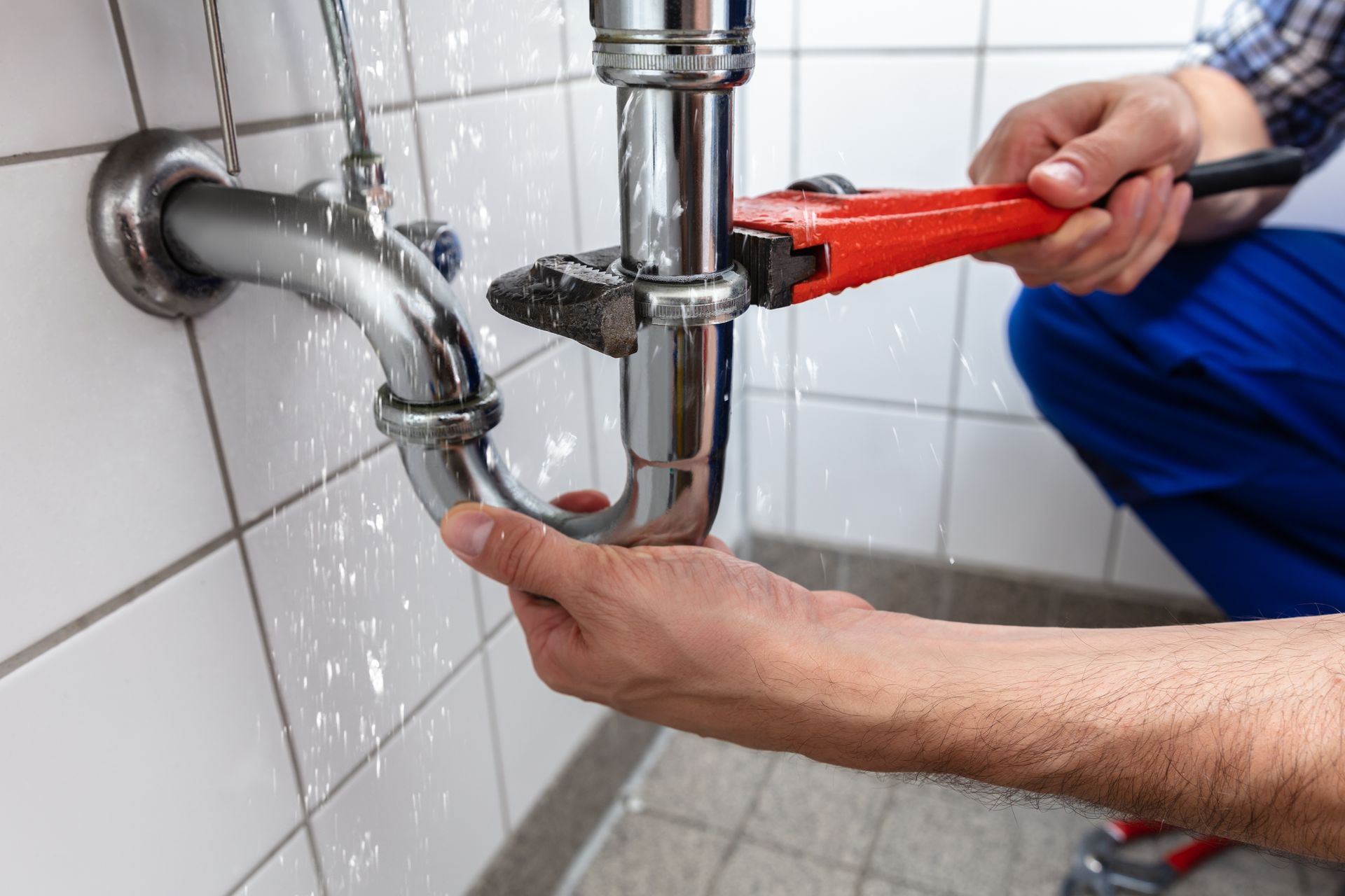 Plumber using wrench to fix a leaking sink pipe in a tiled bathroom.
