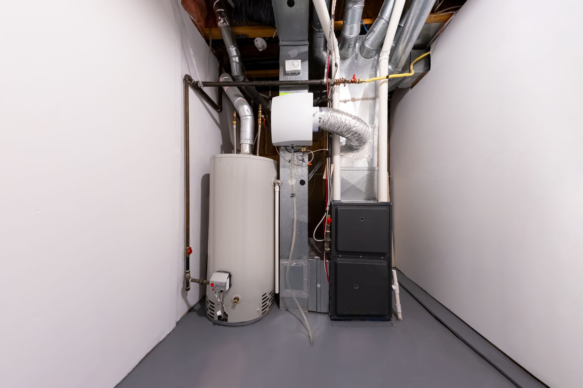 Water heater and furnace in a basement utility room, flanked by white walls and a gray floor.