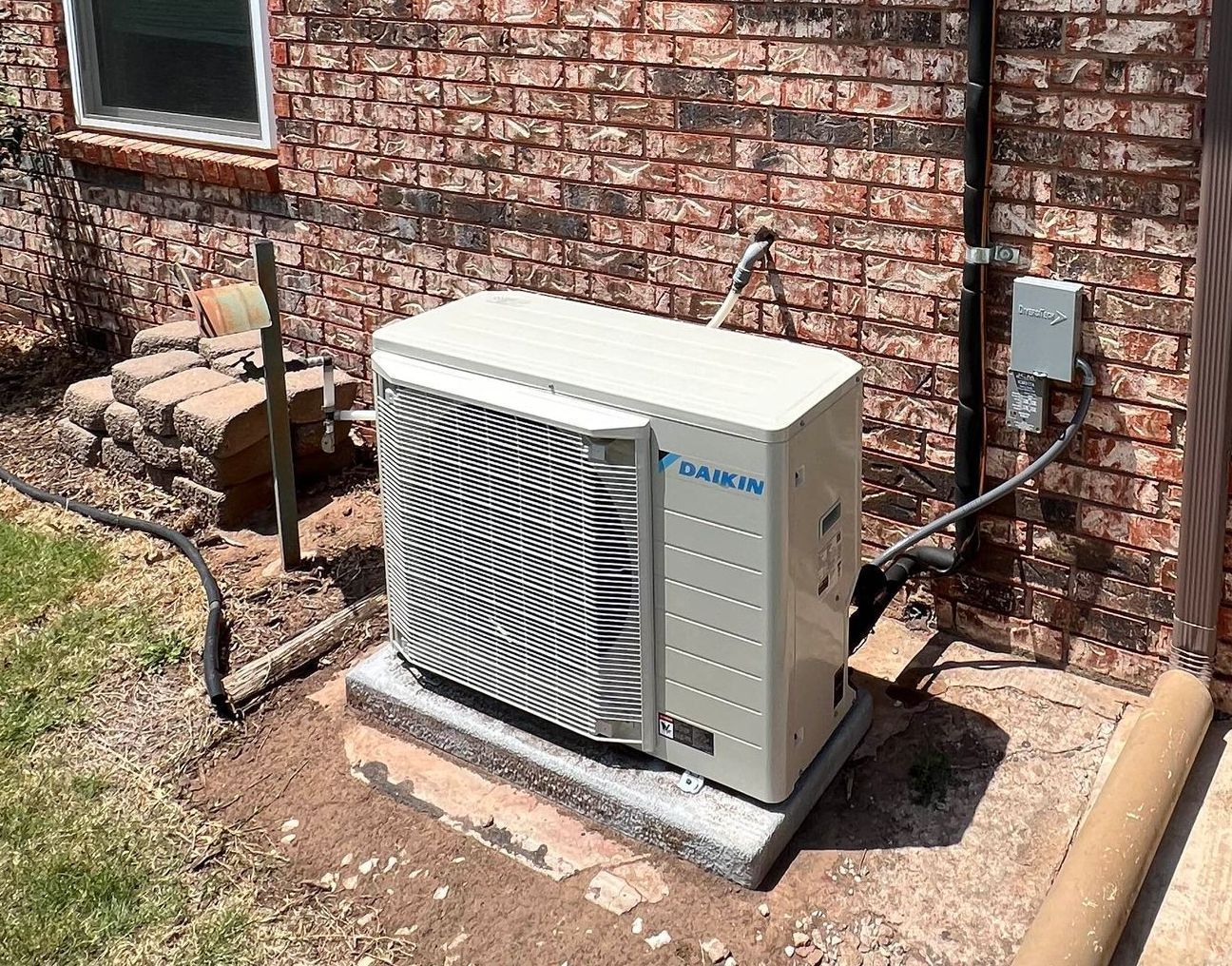 Exterior air conditioning unit on a concrete pad next to a brick wall.