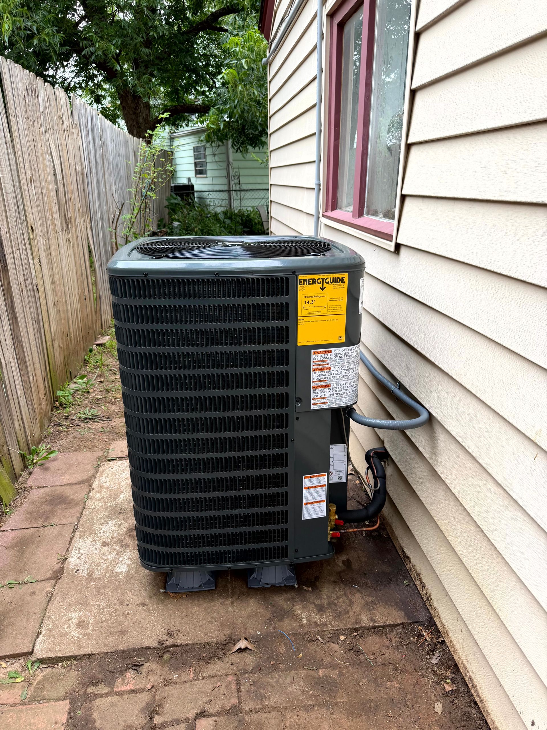 Two outdoor air conditioning units on a brick patio, near a house.