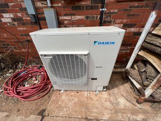 Two outdoor air conditioning units on a brick patio, near a house.