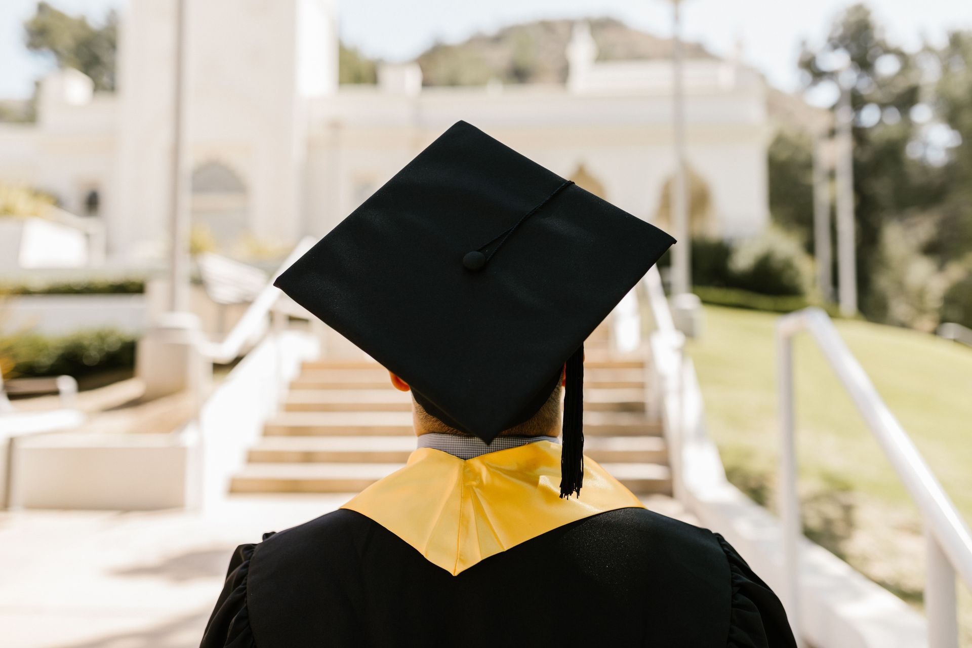 Digital Marketing Agency Partners:
Graduate in cap and gown seen from behind, walking up outdoor campus steps