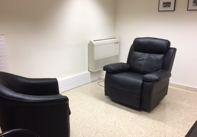 Una habitación con dos sillas y un ventilador en la pared.