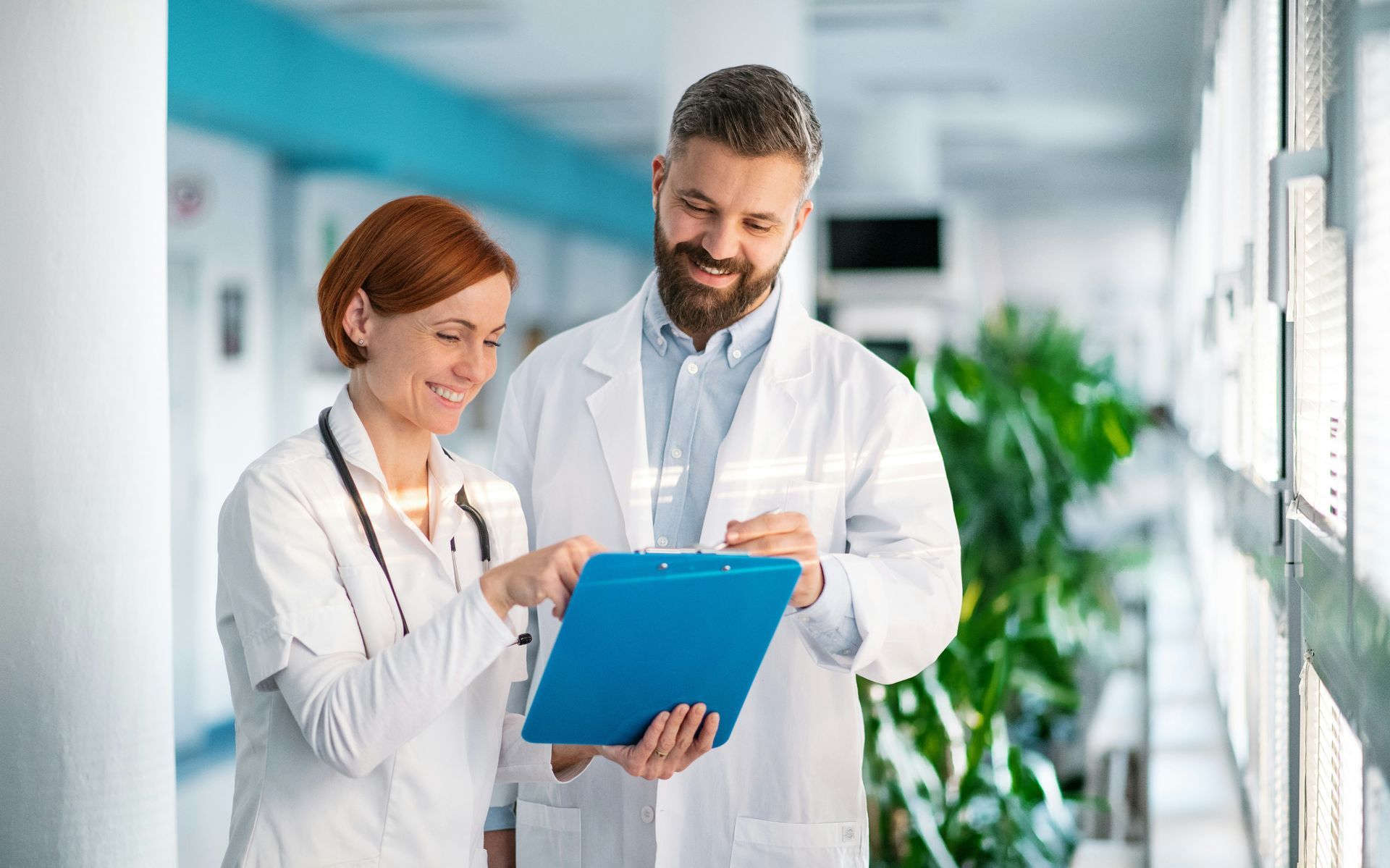 Two medical professionals are looking at a clipboard in a hospital hallway.