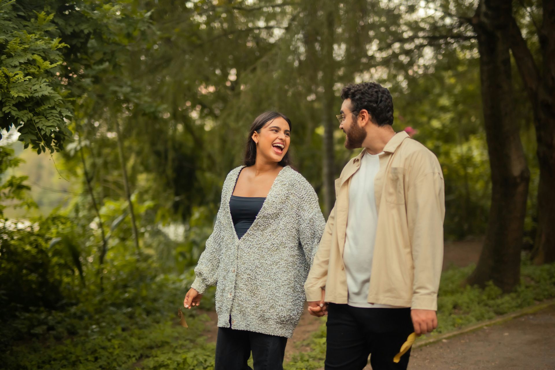 A man and a woman are walking down a path in the woods holding hands.