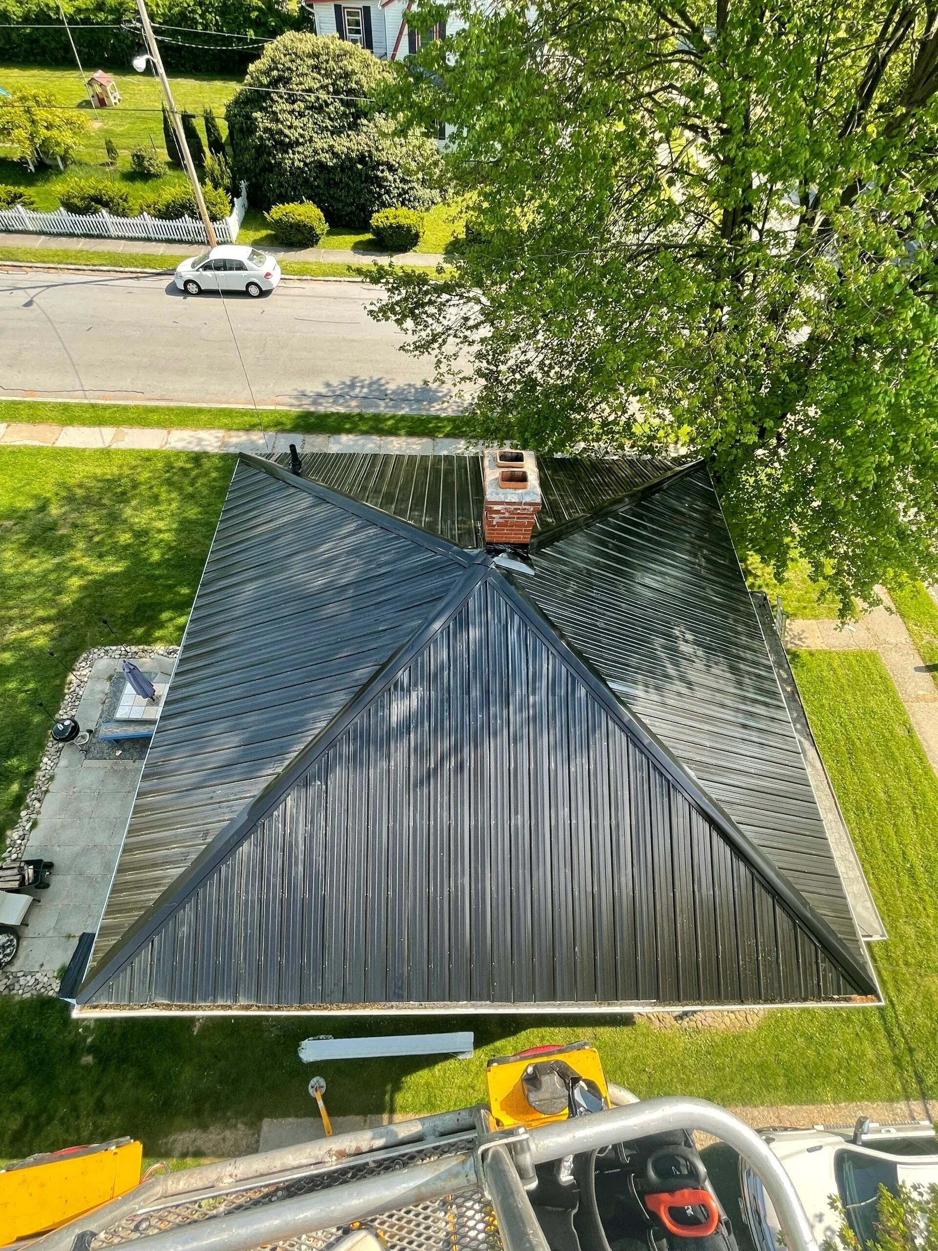 Overhead view of a house with a newly installed black metal roof, chimney, green lawn, and street in view.