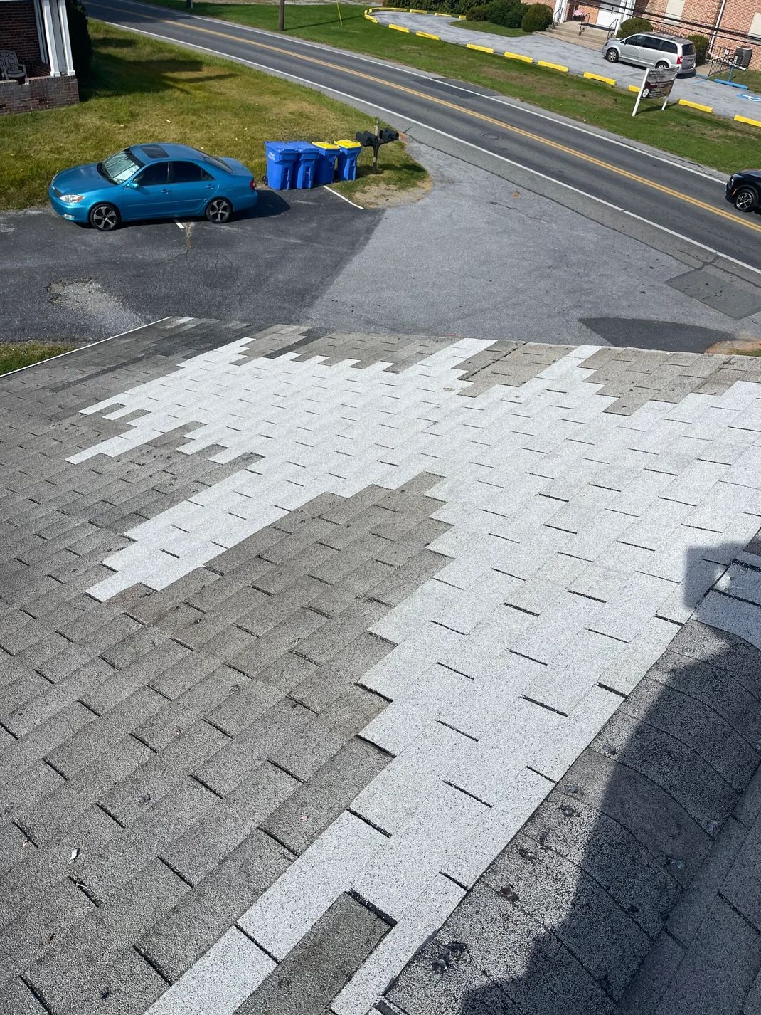 Rooftop with a section of new gray shingles contrasted with old, weathered shingles. Road and parked car in background.