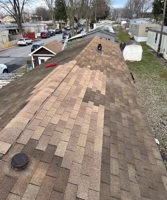 View of a brown shingled roof with missing patches, overlooking a street lined with houses and vehicles.