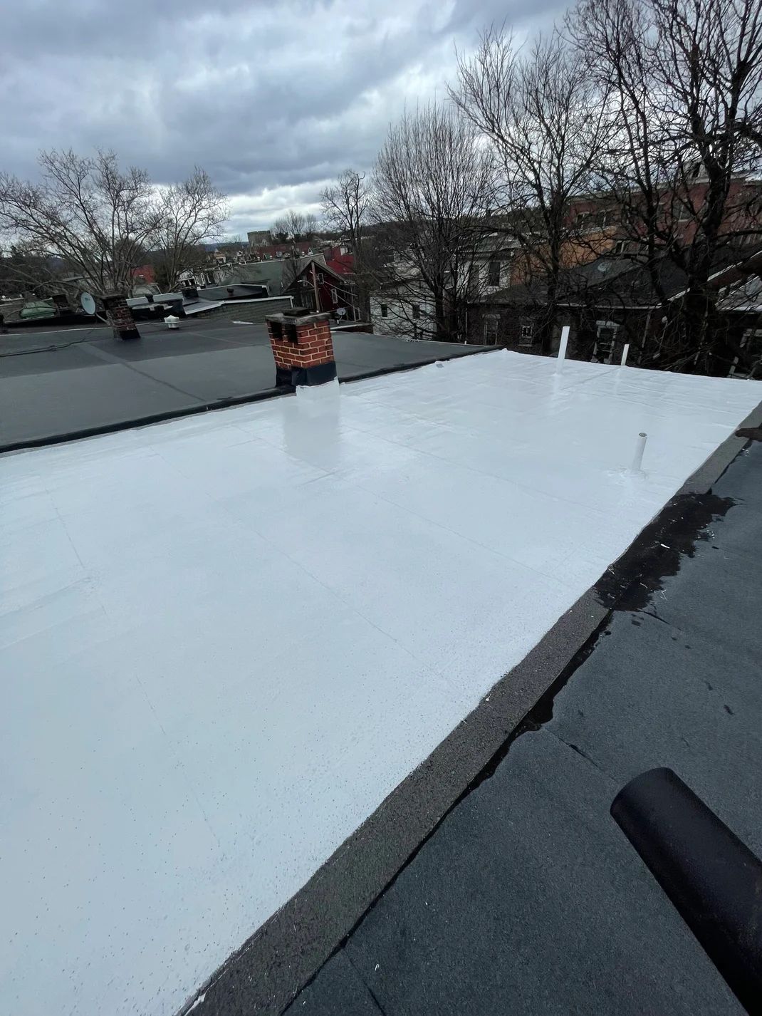 White roof with applied coating, chimney in the center, overcast sky.
