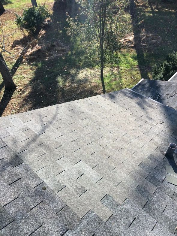 Overhead view of a gray asphalt shingle roof with some missing shingles, trees in the background.