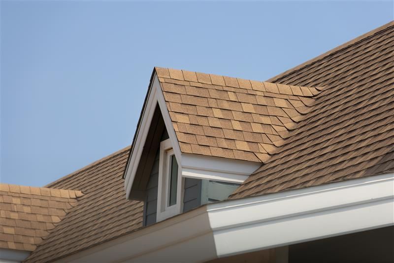 Brown shingle roof with a dormer against a clear blue sky.